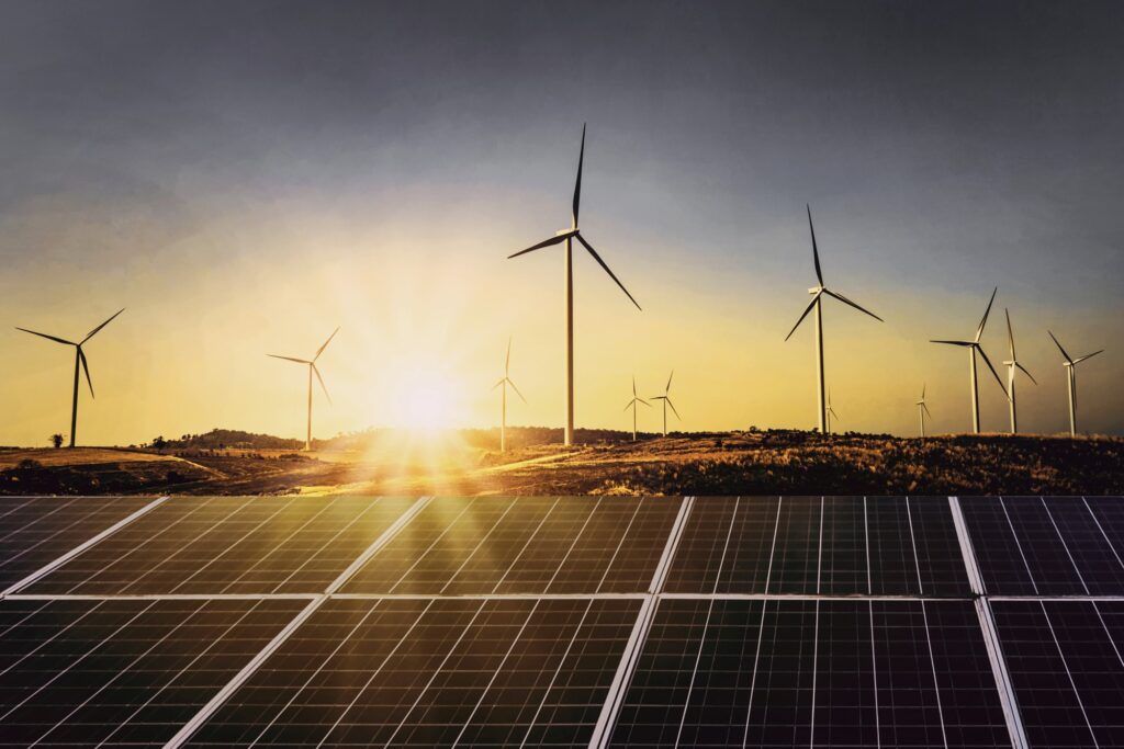 Wind turbines and solar panels sit in the foreground of a sunset.
