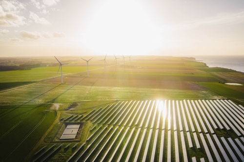 The sun shines over a solar and wind field.