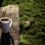 A white mug of coffee on a park bench